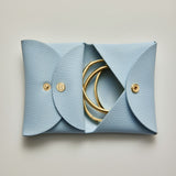 Blue leather jewelry pouch with gold rings on a light gray background